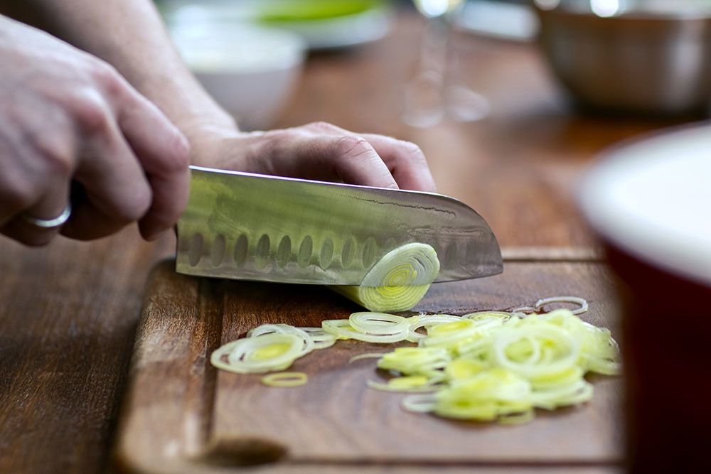 Male hands holding sharp knife cutting leeks