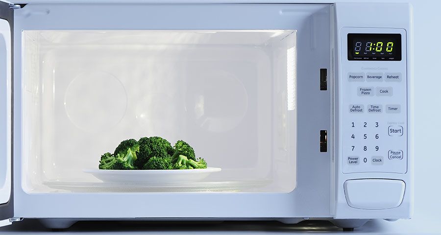 Open microwave with white plate of broccoli inside